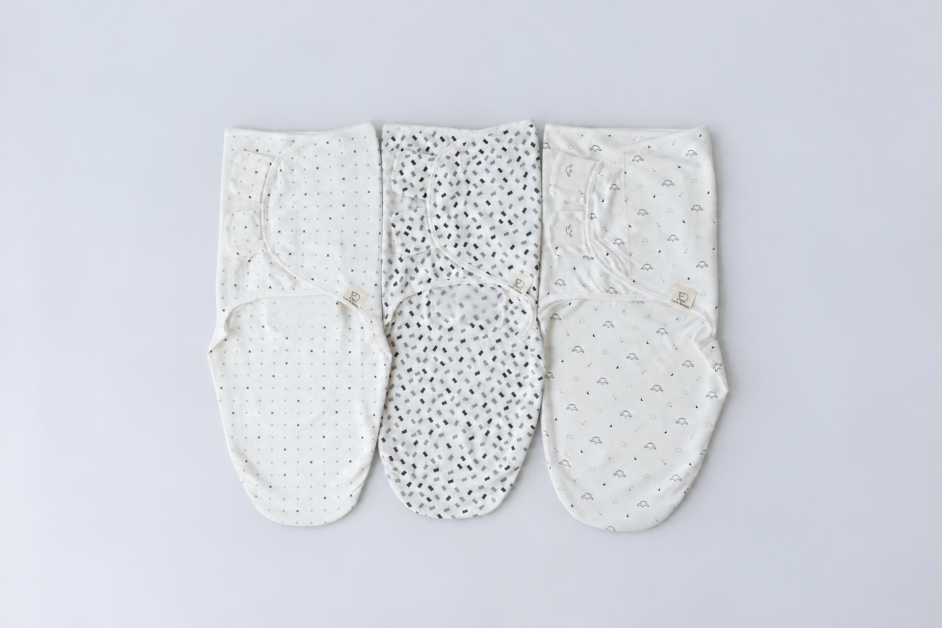 Three white Lamb Babies swaddle wraps with gray prints laid close together on a soft gray studio backdrop