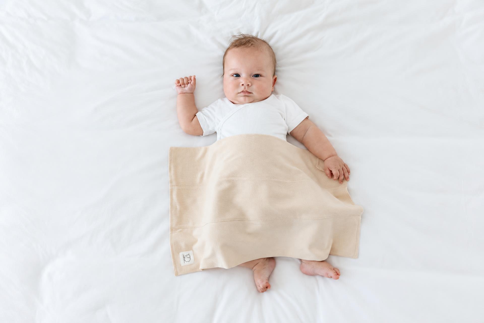 Baby lying on a white bed under a soft sand-colored blanket with the Lamb Babies label