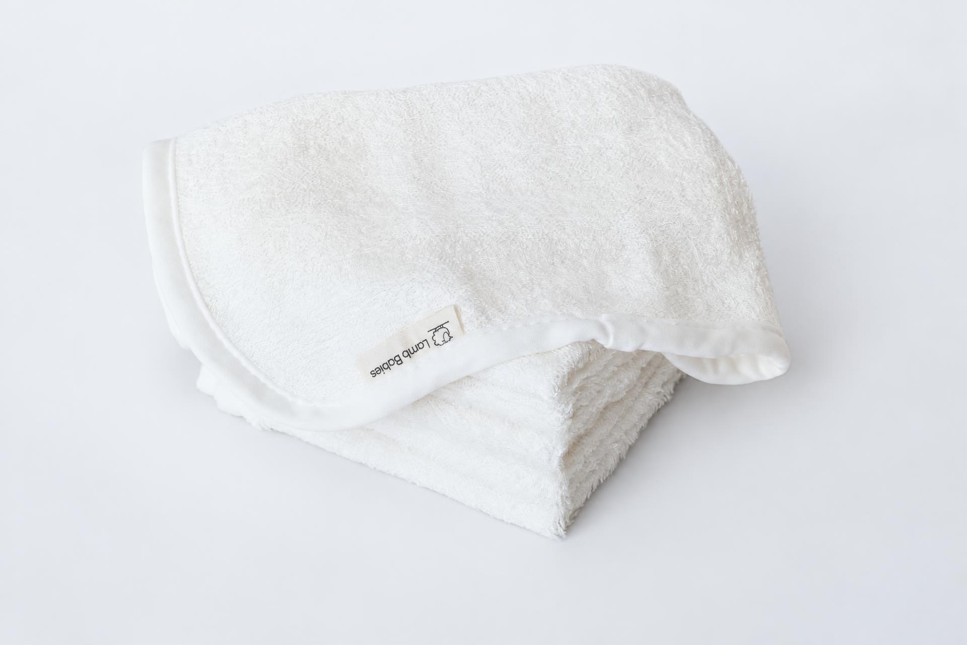 Lamb Babies white baby washcloths, folded stack on a soft gray studio backdrop