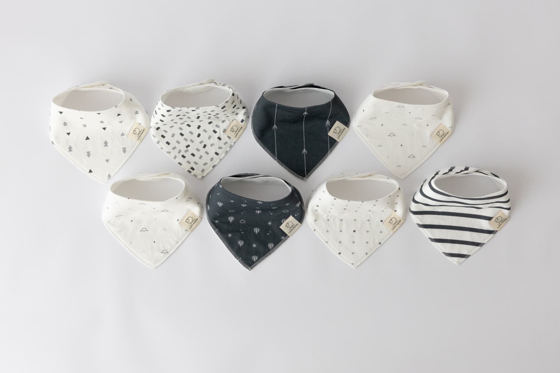 Lamb Babies pattern bandana bibs, eight bibs laid flat in two rows showing the prints
